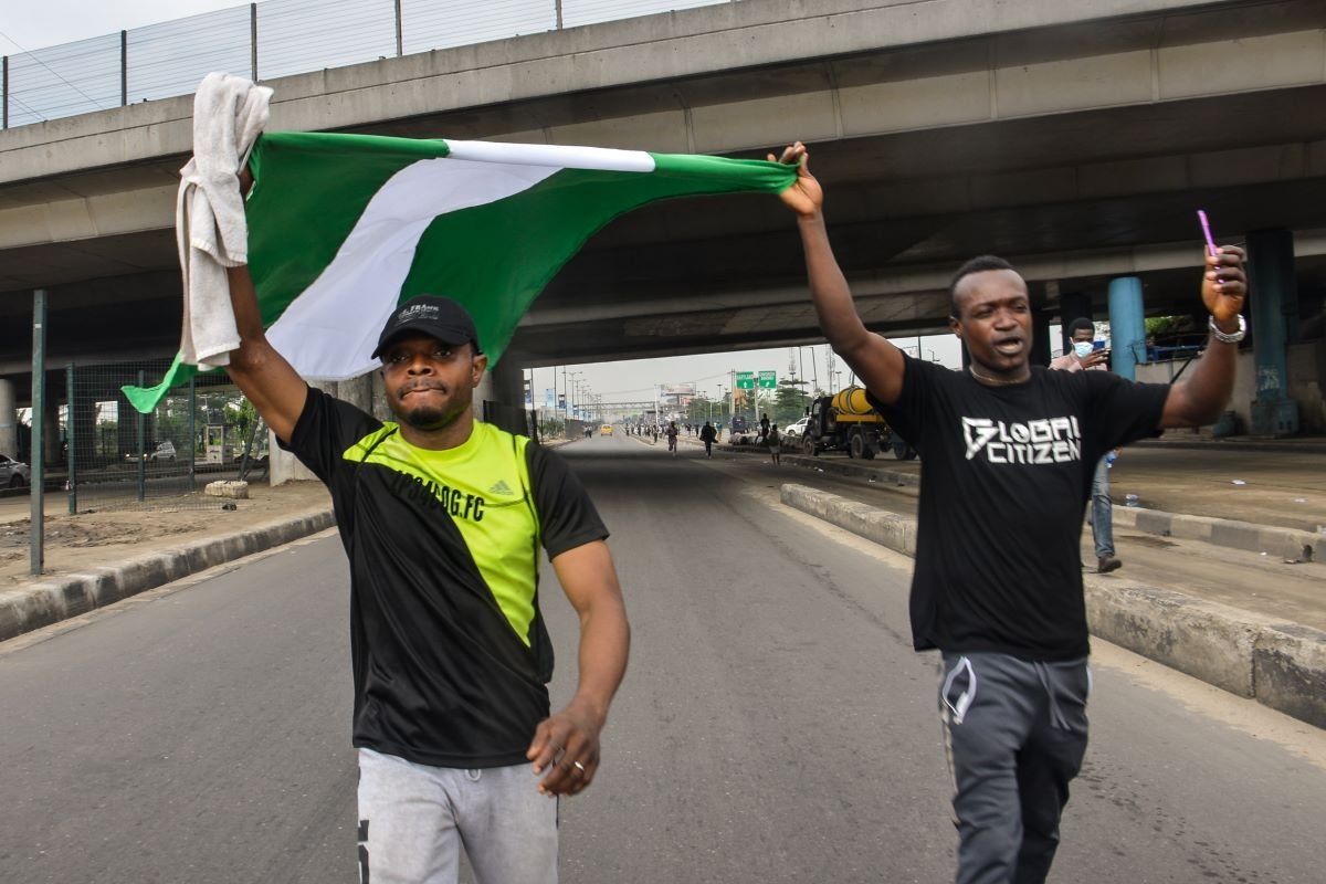 A photo of two protesters holding the Nigerian flag on the road.