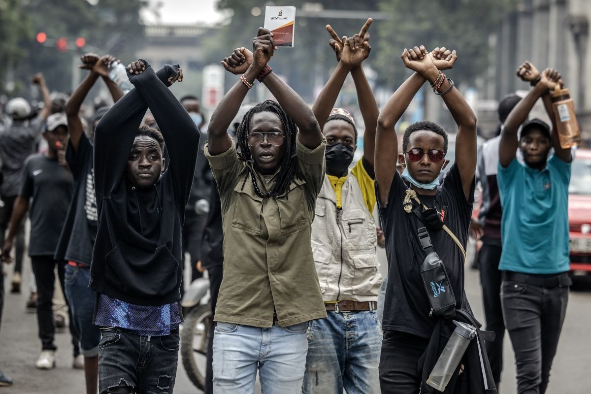 Protesters make signs with their arms in front of Kenya police officers during a demonstration against tax hikes as Members of the Parliament debate the Finance Bill 2024 in downtown Nairobi, on June 18, 2024.
