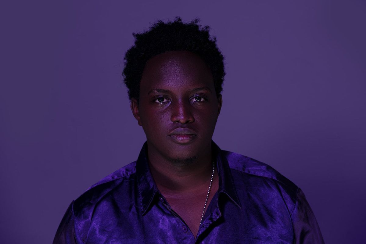 Ugandan artist Joshua Baraka poses in a purple shirt.