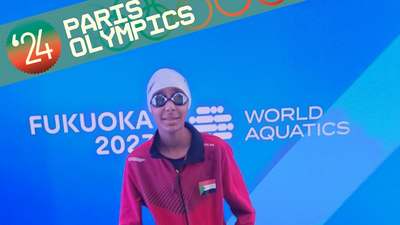 Rana Saadeldin standing in front of the blue World Aquatics Championships banner, wearing goggles. 