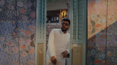 Soulja standing inside a green door frame, rapping. To his left and right are colorful walls with flower print. 