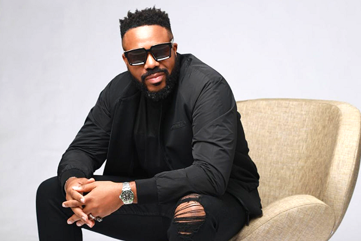 Man sitting in sunglasses, black jacket and ripped jeans.