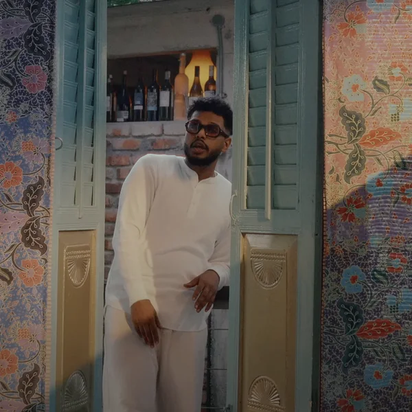 Soulja standing inside a green door frame, rapping. To his left and right are colorful walls with flower print. 